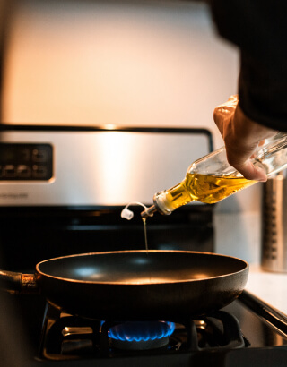 A pan on the stove with someone pouring in oil
