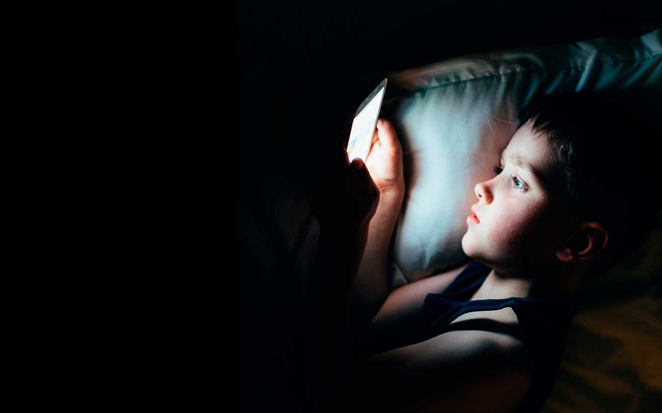 Child using a phone in bed in the dark