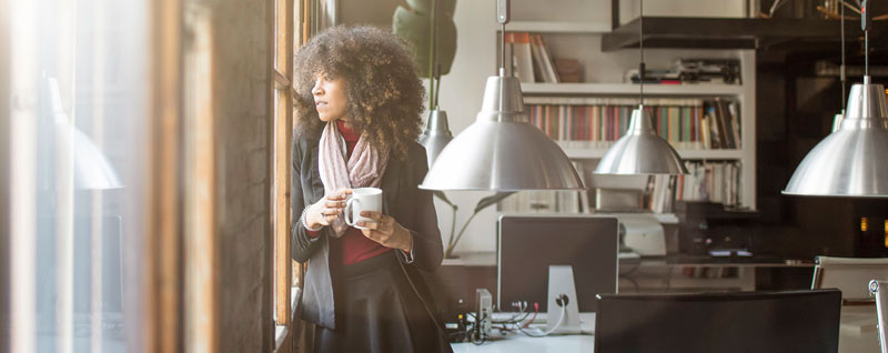 Lady in office holding mug looking out of window