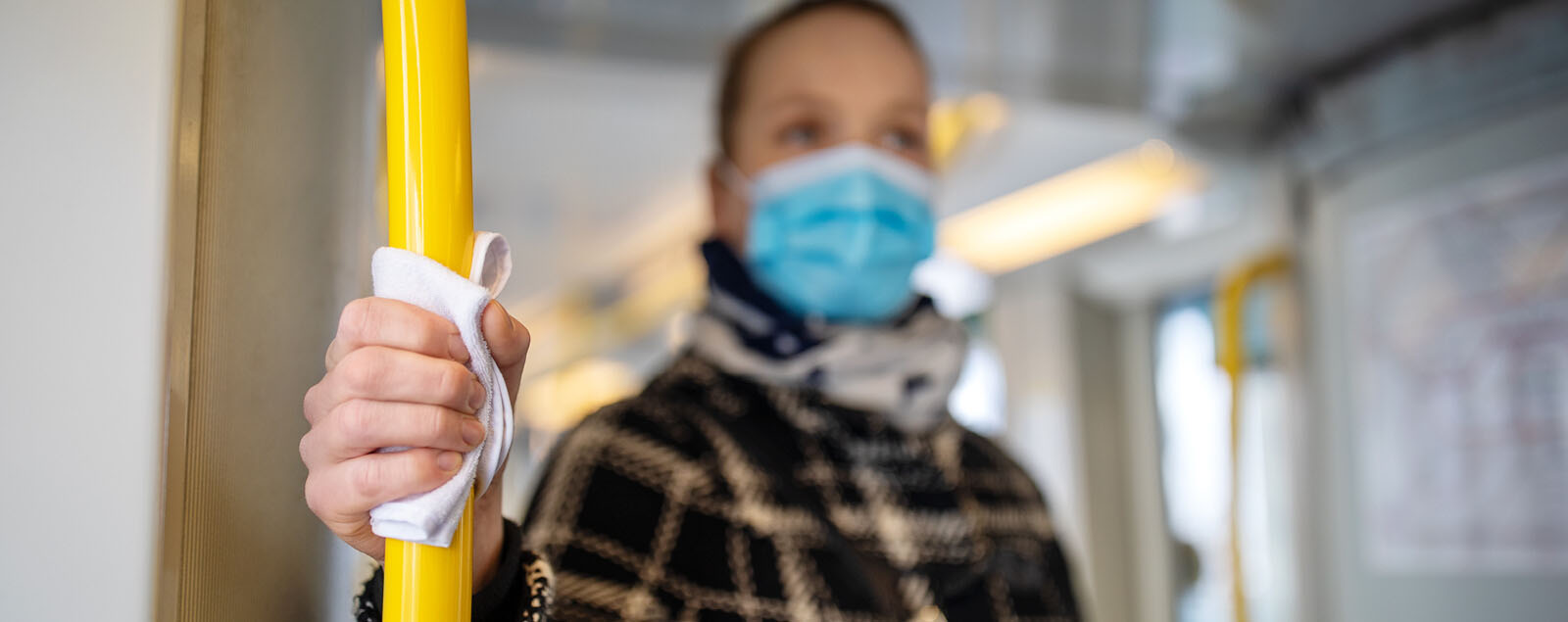 Lady wearing mask on train holding support bar with cloth