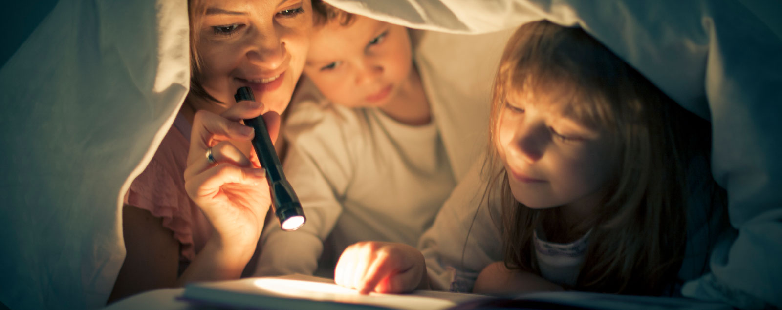 Mother and children under duvet reading with torch