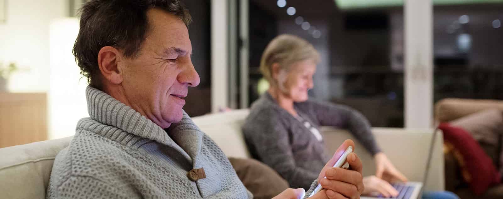 Man using smartphone with partner using laptop