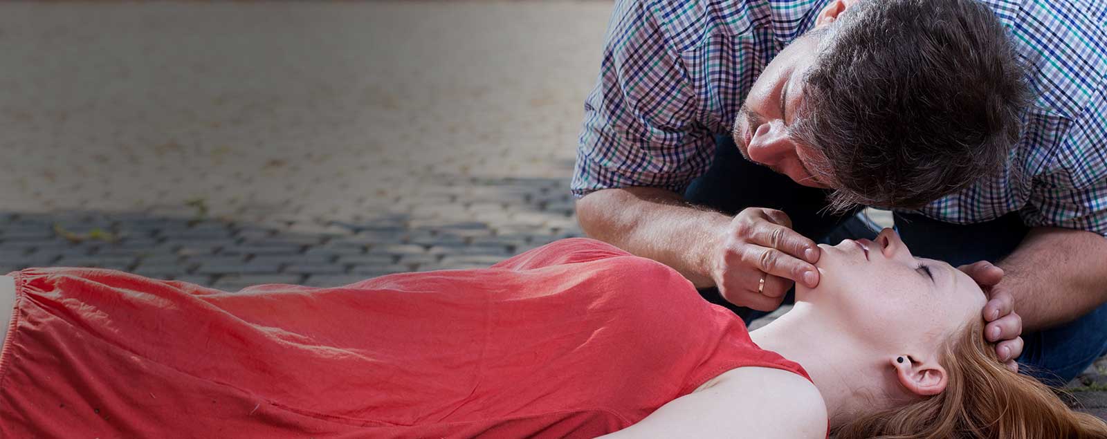 Emergency situation of unconscious lady and man with hands on her head and ear to her face