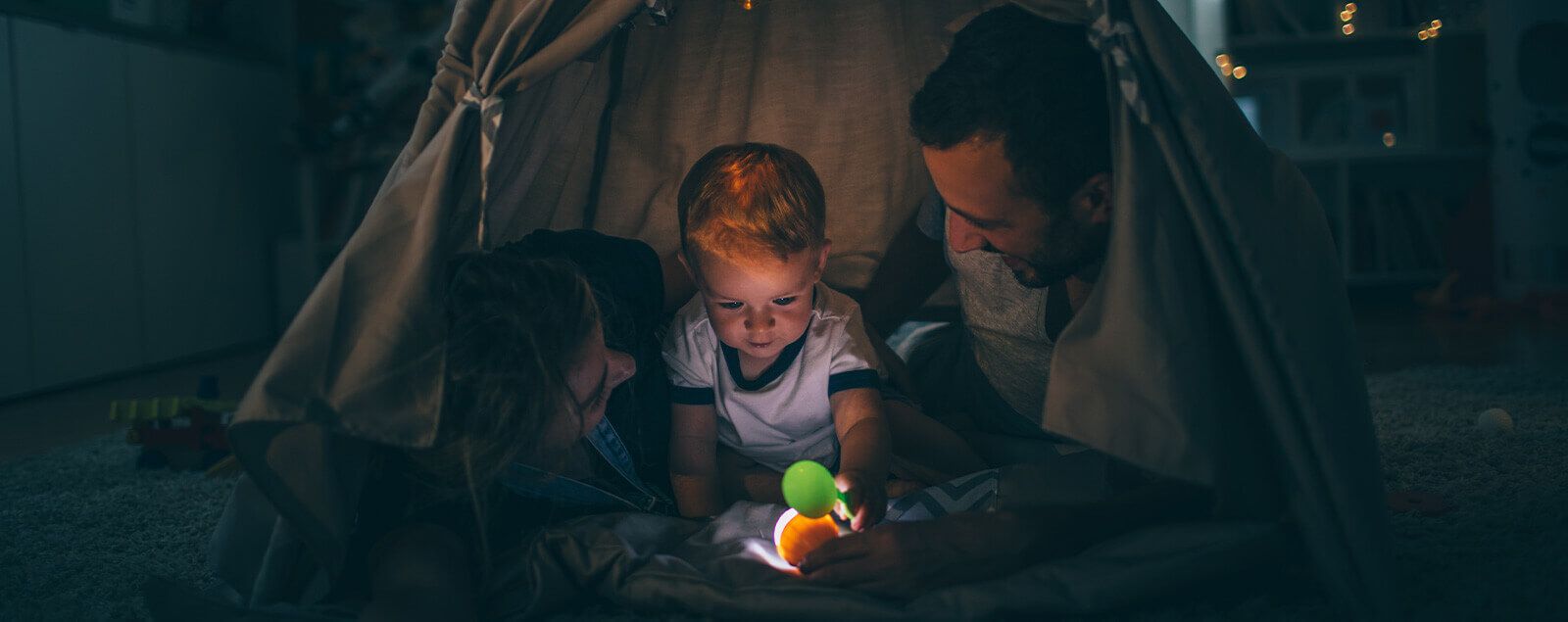 Parents and son in tent fort at night with torch
