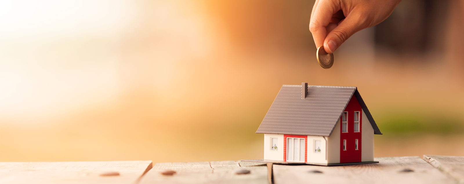 Model house with hand placing coin over it