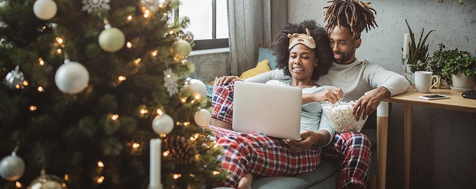 Couple on sofa using laptop with Christmas tree in foreground 