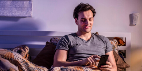 Man sat up in bed using smartphone