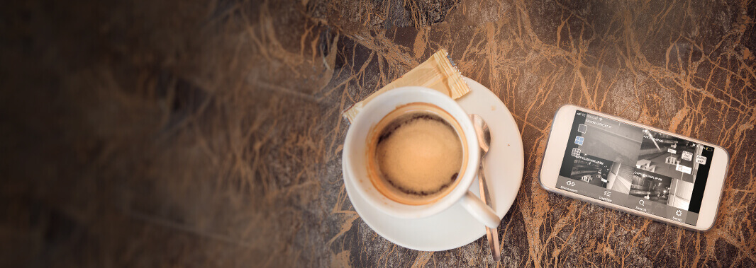 Table with cup of coffee and a smart phone device showing CCTV camera footage