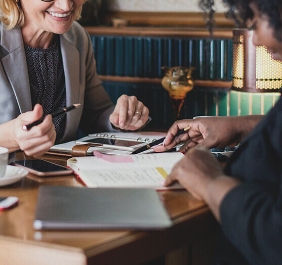 Two ladies at table with pens and notebooks talking