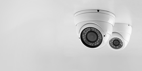 Two white, wall-mounted security cameras with lights
