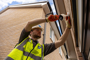 Man in hardhat and hi-vis installing security camera on exterior wall