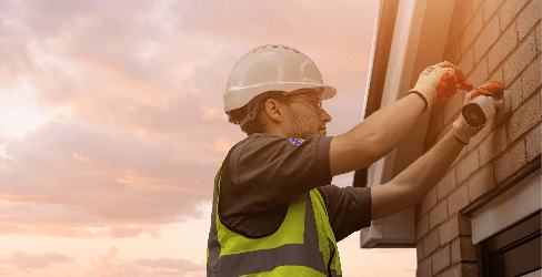 Man in hardhat and hi-vis installing security camera on exterior wall