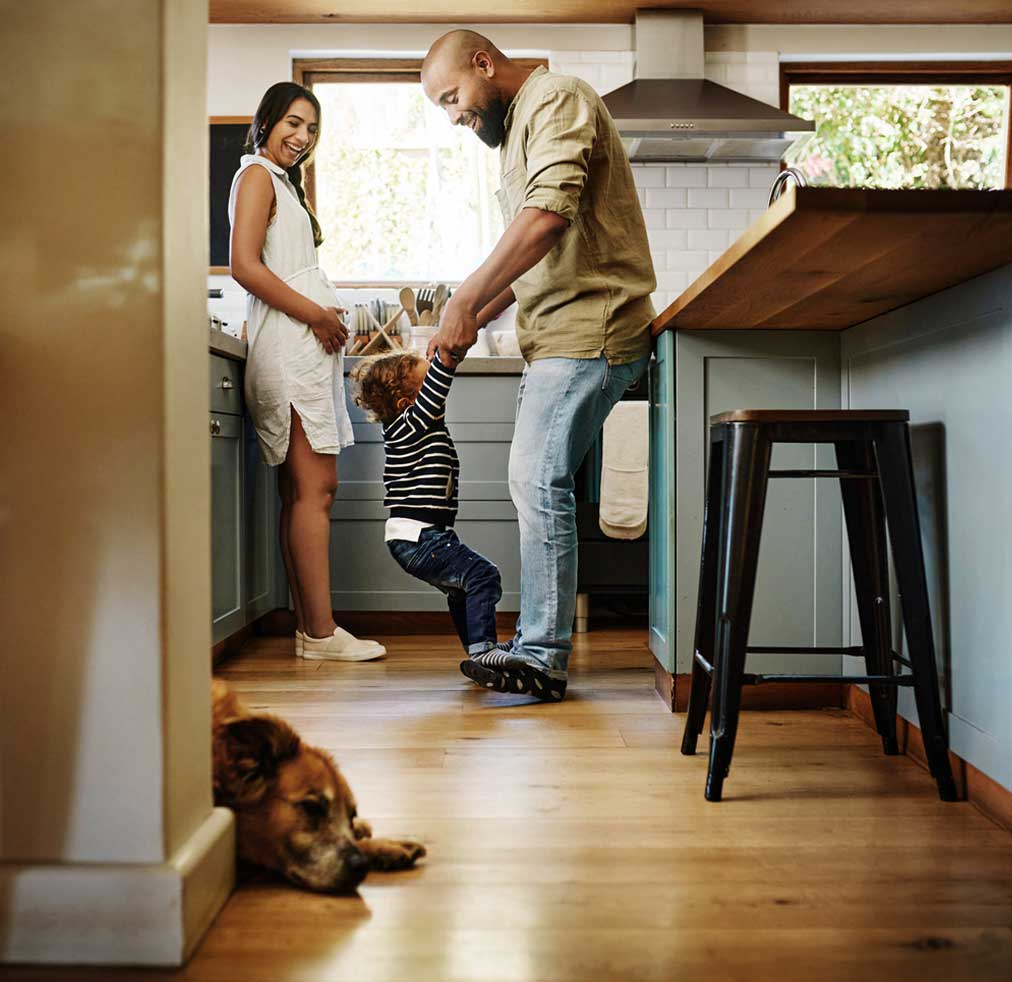 Parents playing with child in kitchen, dog sleeps on floor