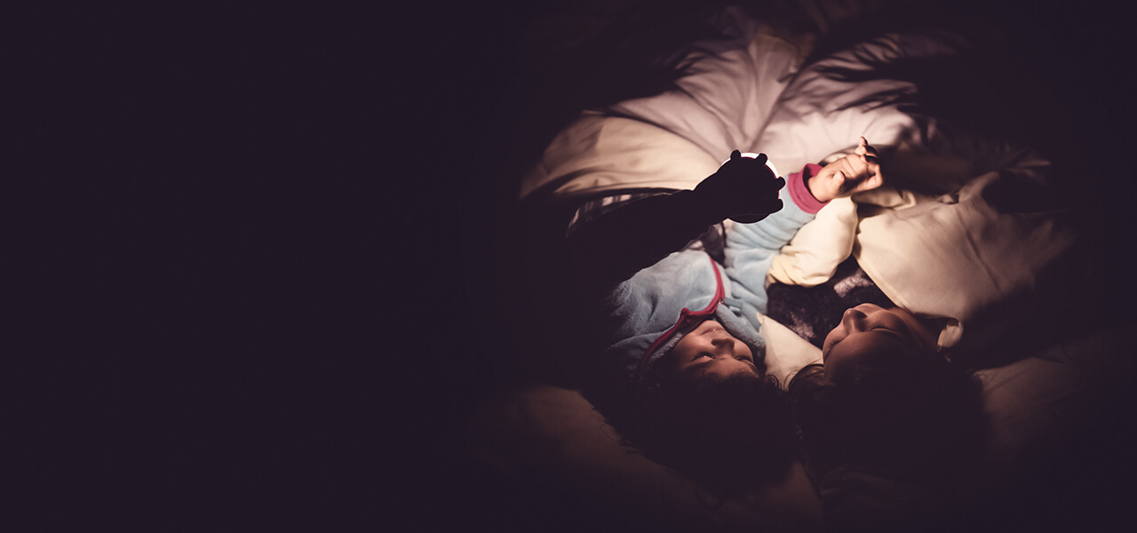 Two children in sleeping bags at night with lamp