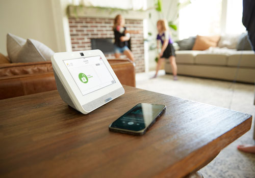 ADT security control panel on table next to smart phone with children playing in background