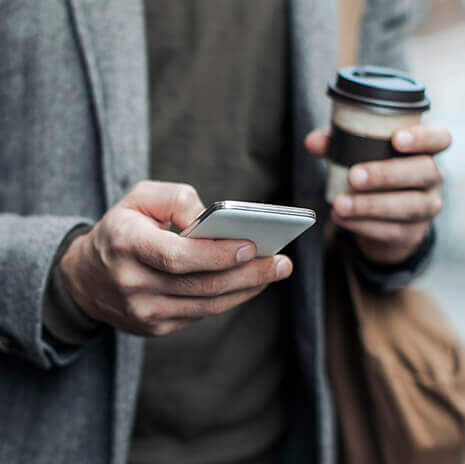 Torso shot of man holding hot drink and smartphone