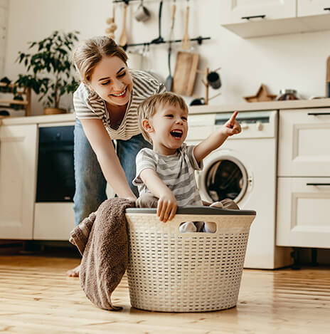 Child playing in washing basket with mother behind
