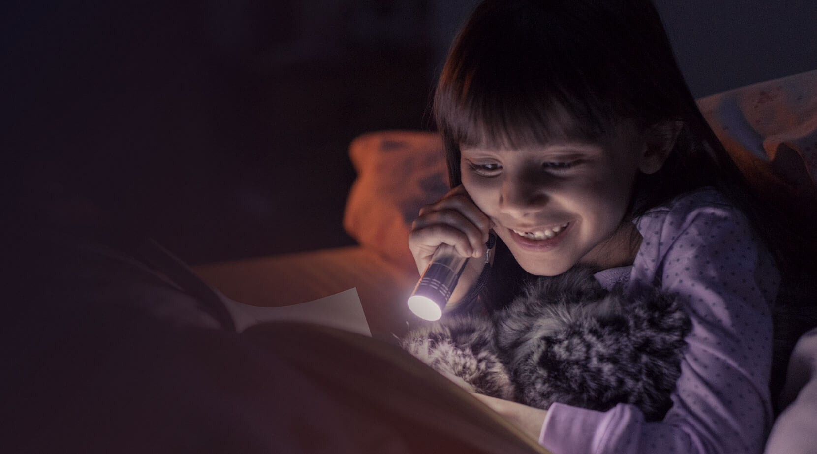 Girl in bed at night reading with torch